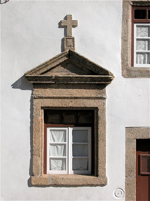 Window with elaborate granite surround with roof shape and cross in Marvao